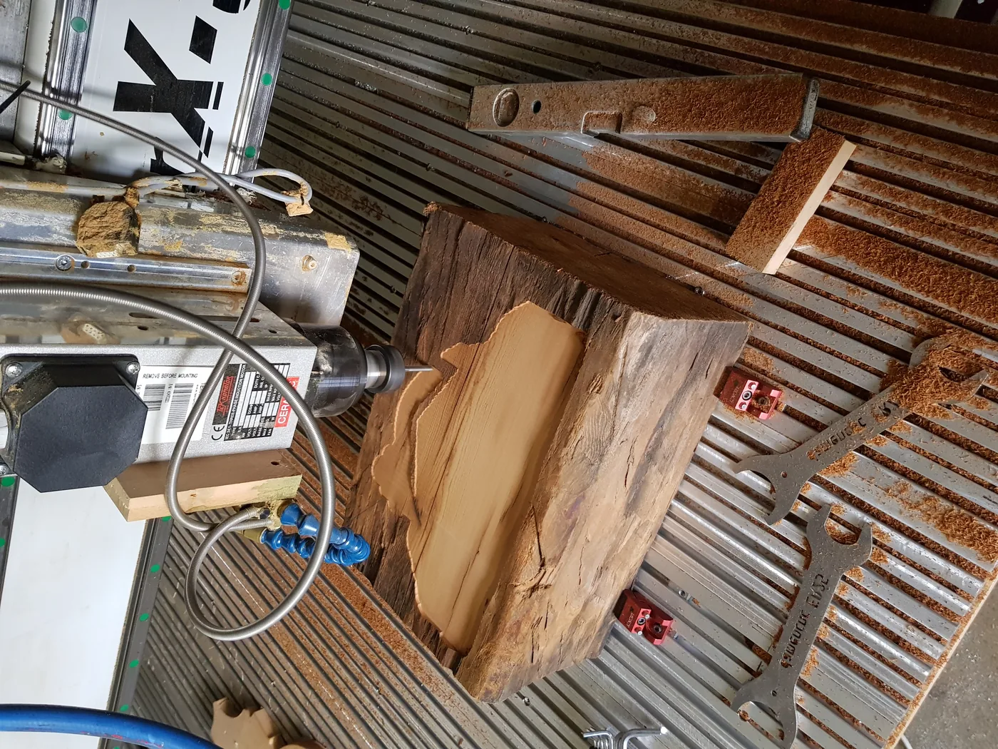 Altholzbalken auf dem Frästisch, aus dem in groben Bahnen die Umrissform des Motivs ausgeräumt wird